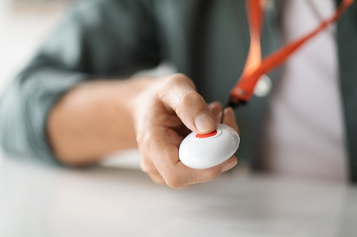 Unrecognizable senior man pushing panic button on emergency equipment for elderly people hung on his chest, closeup shot of male hand pressing alarm button for quick help, cropped image