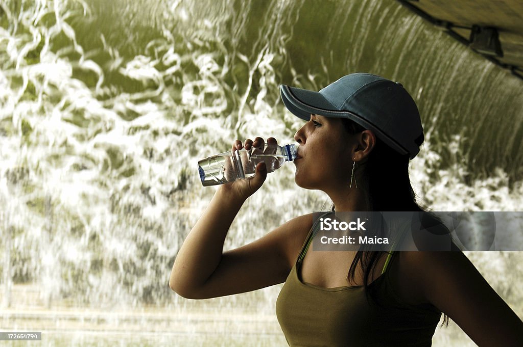 Fresh water "Young woman drinking water at a park, in front of a waterfall." Adolescence Stock Photo