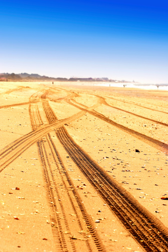 Tyre tracks run across a sandy beach on a bright summers day.