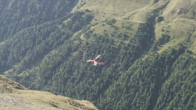 Swiss resque helicopter flying upward through alpine valley