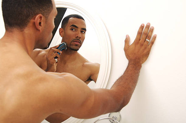 istock Man shaving while looking at the mirror and holding wall 172660834