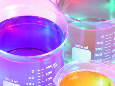 Close up of colorful liquids in test tubes and glass laboratory flasks on a pink yellow gradient background. Empty podium for product display with laboratory space.