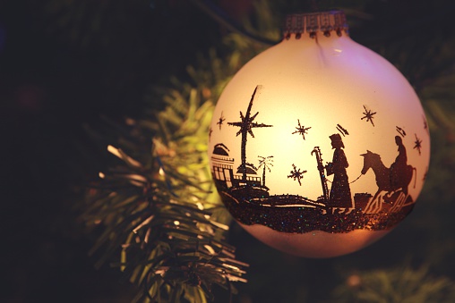 Christmas Ornament with silhouette of nativity scene with Mary, Joseph, and Bethlehem. Ornament is hanging from branch of tree. Horizontal image would be good for Chistian or religious use.