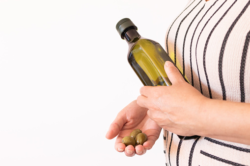 woman's hand with some olives and a bottle of extra virgin olive oil.white background with copy space.inflation concept in economy and food.typical mediterranean diet and spanish culture.