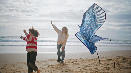 Mother son launching kite on windy ocean shore. Cheerful woman helping child with toy on autumn weekend. Excited little boy playing rest beach with babysitter. Supportive loving family relationships