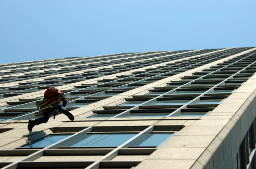 A man hanging in a harness and fixing windows on a tall building.