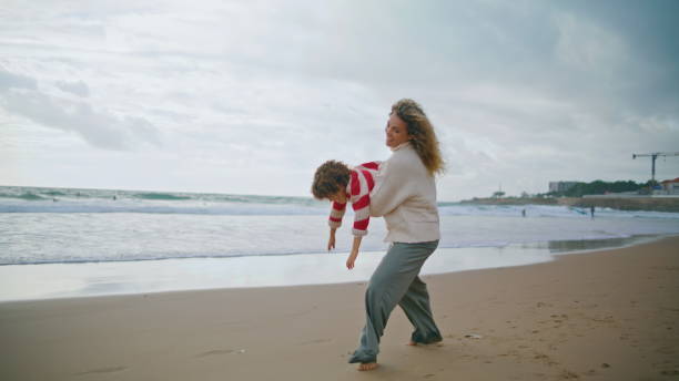 istock Joyful mom spinning kid on autumn beach. Smiling babysitter playing airplane 1726650495
