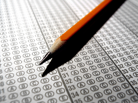 A close up of an optical scan exam answer sheet and a pencil. The answer sheet was desaturated of color; it is in b&w, with contrasting yellow pencil.