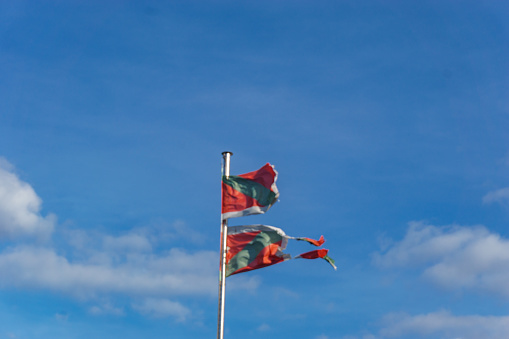 Torn Basque country flag Ikurrina with blue cloudy sky