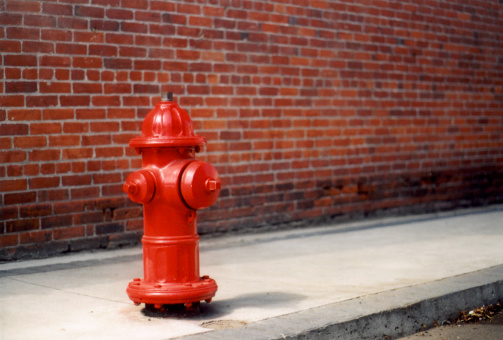 A vibrant red fire hydrant stands prominently against a neutral urban background. The silver top contrasts with the bright red body, emphasizing its functionality and importance.