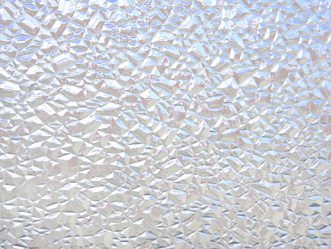 This color photo shows an interesting frosted glass texture, consisting of diamond-like, multifaceted sections. Overall image has a grayish appearance with white highlights from light striking certain facets.