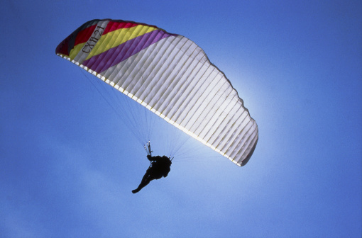 Paragliding on the island of Sardinia. White paraglider against the sun and the blue sky.