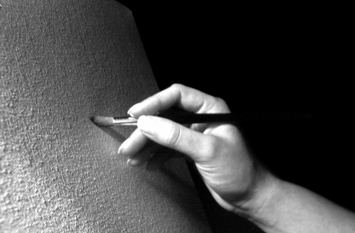 A hand painting a canvas with a black background. Ideas: replace or put on the canvas any subject of your own.