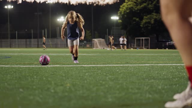 Little girl kicking a ball at a goalie during a soccer practice