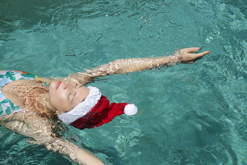 Young woman in santa hat relaxing in swimming pool. Christmas tropical vacation concept.
