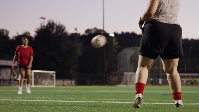 Smiling young woman kicking a ball at a goalie during a soccer practice