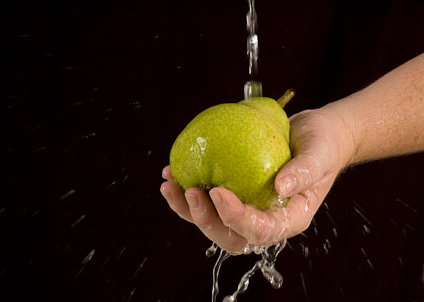 Washing Pear Rinsing a pear under stream of water against black. perfect pear stock pictures, royalty-free photos & images