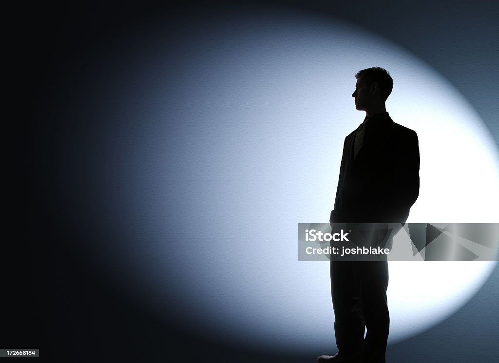 Businessman silhouetted in a spotlight businessman looks sideways. Spot Lit Stock Photo