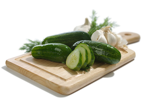 Pickles, garlic, and dill on a cutting board.