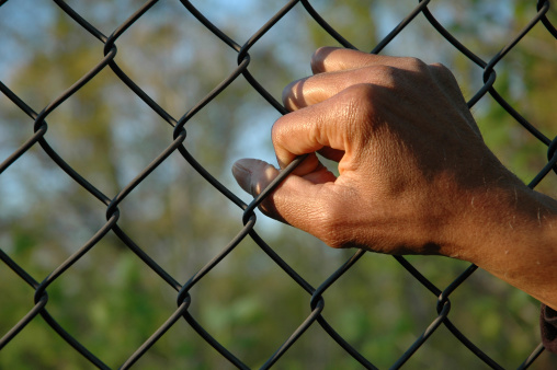 A male African-American hand clings to a chain link fence.