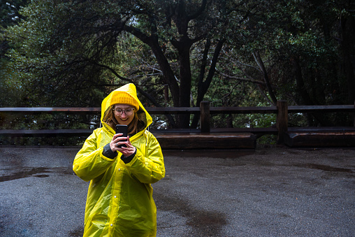 Smiling woman hiker in yellow raincoat standing and taking photo in Yosemite Valley