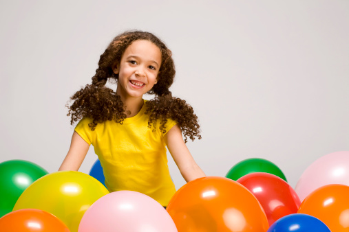 Cute little girl playing in a bunch of colorful balloons.