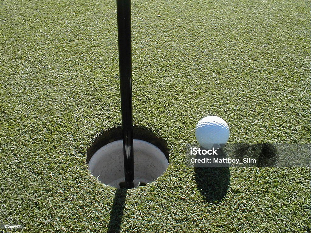 Close up of golf ball and cup A close up shot of the green with the golf ball resting beside the cup. Hole Stock Photo
