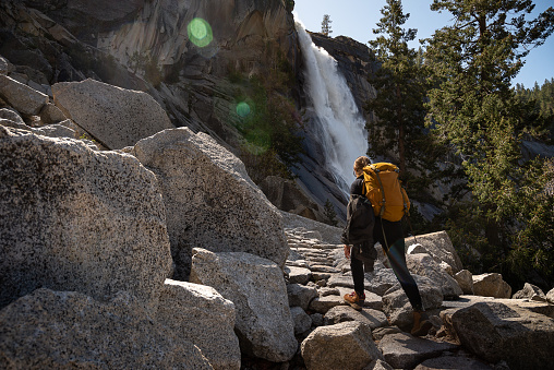 Woman hiker with a yellow backpack on her back climbing a stone path next to Nevada Fall