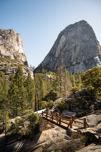 View of Half Dome and a woman hiker on the Merced River wooden bridge of the Mist Trail in Yosemite National Park