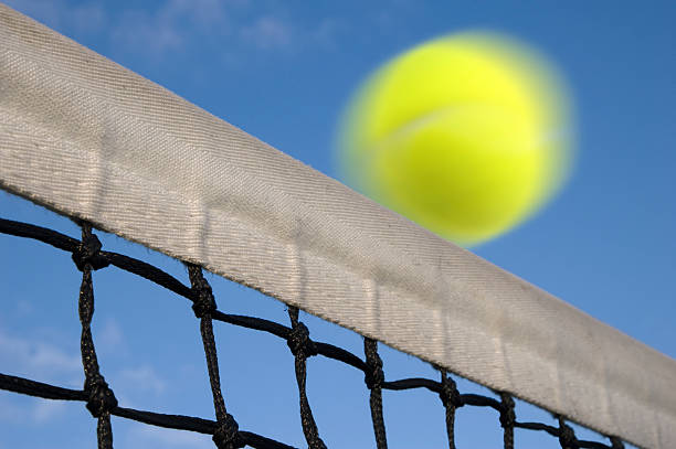 Tennis ball flying over net stock photo