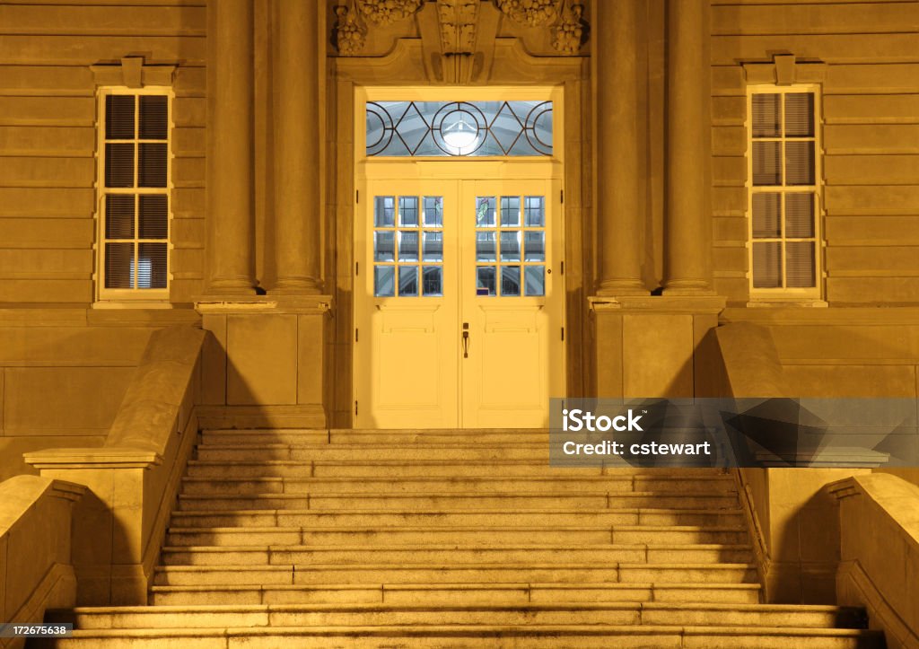 Floodlit Entrance to College Building at Night Streetlamps cast an eerie glow on the entrance staircase and door to an old building on a college campus. Adult Student Stock Photo