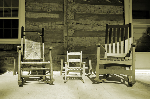 three rocking chairs on a country log cabin porch in sepia