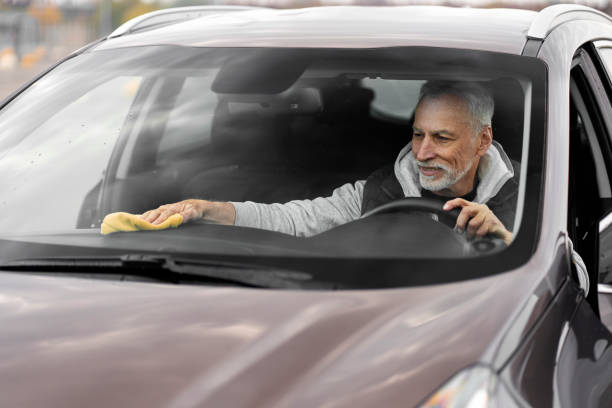 vista a través del parabrisas a un hombre de 60-70 años en el asiento del conductor, limpiando el interior del automóvil con microfibra - senior adult 60 65 years people occupation fotografías e imágenes de stock