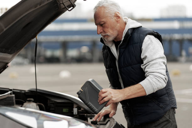 senior man driver checking the oil level and adding motor oil in the engine - old men car oil imagens e fotografias de stock