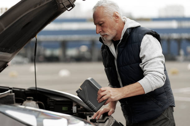 старший водитель проверяет уровень масла и доливает моторное масло в двигатель - old men car oil стоковые фото и изображения