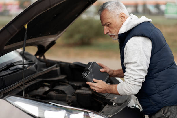 опытный старший водитель-мужчина добавляет экологически чистое масло в двигатель автомобиля перед поездкой - old men car oil стоковые фото и изображения