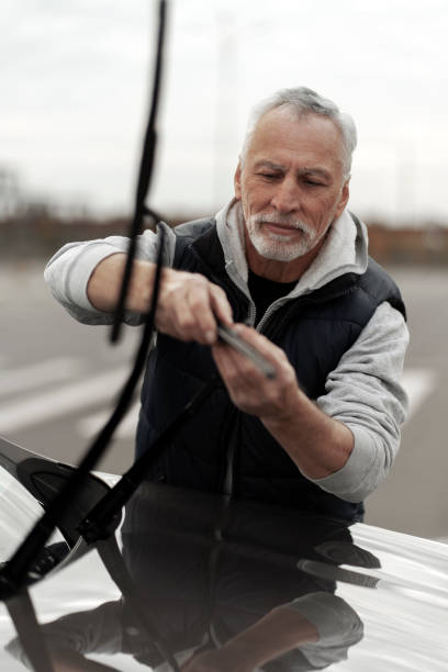 vertical lifestyle portrait of senior man replacing windshield wipers blades on dealership station. - old men car vertical imagens e fotografias de stock