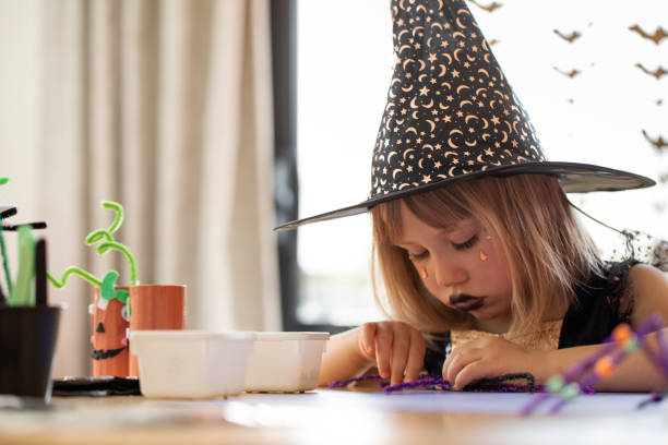 uma garota fofa em uma fantasia de bruxa faz uma aranha engraçada para o halloween com suas próprias mãos. artesanato infantil para o halloween - child autumn craft preschooler - fotografias e filmes do acervo