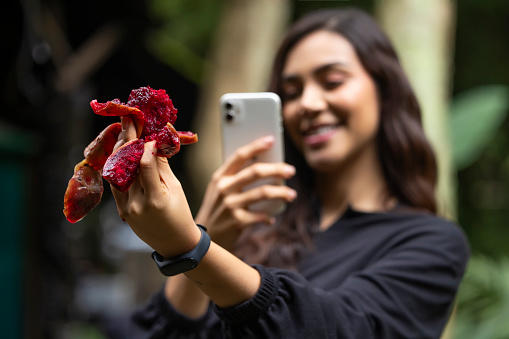 Young woman taking a picture of a red fruit