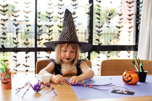 uma garota fofa em uma fantasia de bruxa faz uma aranha engraçada para o halloween com suas próprias mãos. artesanato infantil para o halloween - child autumn craft preschooler - fotografias e filmes do acervo