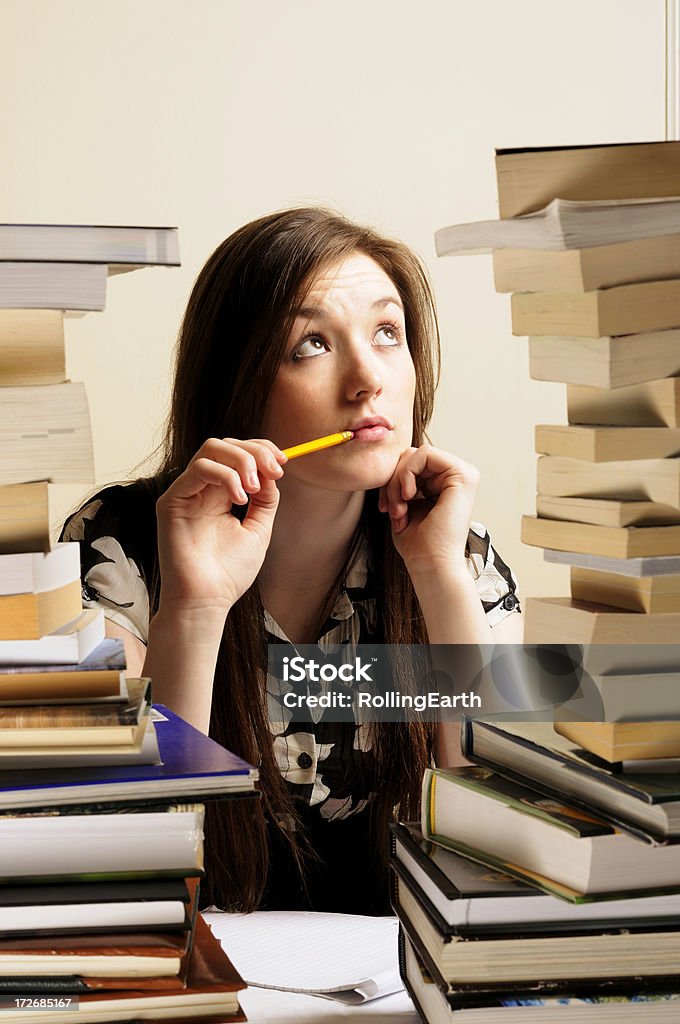 Study A beautiful young woman sitting at a desk with two large piles of books. Pencil Stock Photo