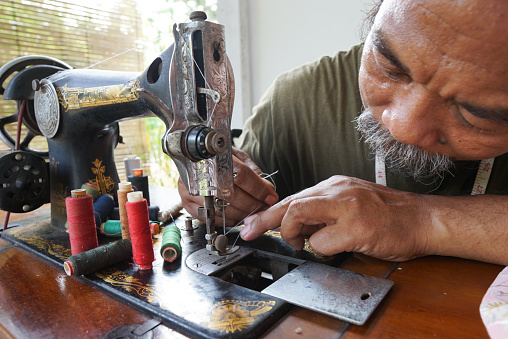 A senior tailor sits and sews on a sewing machine. Dressmaker work on the sewing machine.