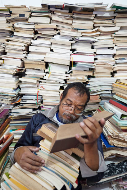 Lecturer reading a book in the university library, looking exhausted and tired from studying. Sleeping on stacks of books