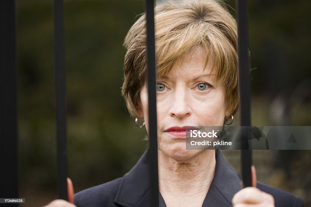 Woman sad behind bars Close up of woman who looks sad standing behind bars. Adult Stock Photo
