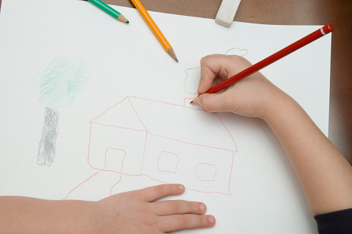Child drawing a house with color pencils.