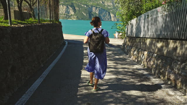 SLO MO Female Tourist With Backpack Walking Towards Lake Garda Surrounding Mountains on Sunny Day