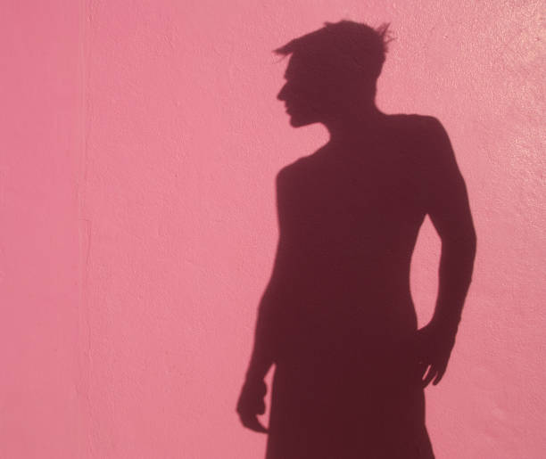 Shadow man stands in profile with his back against pink wall