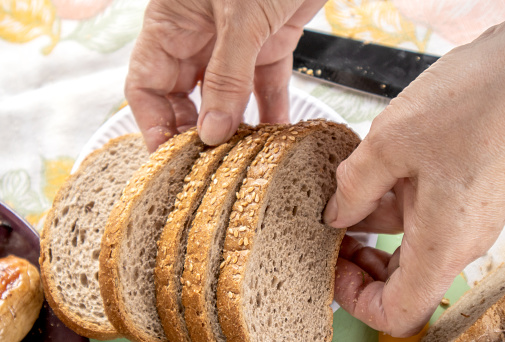 Women's old hands hold slices of whole grain bread with sesame seeds, close-up, selective focus.