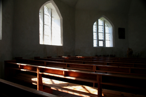 You see a small church with wooden interior. The sun shines through the old windows.