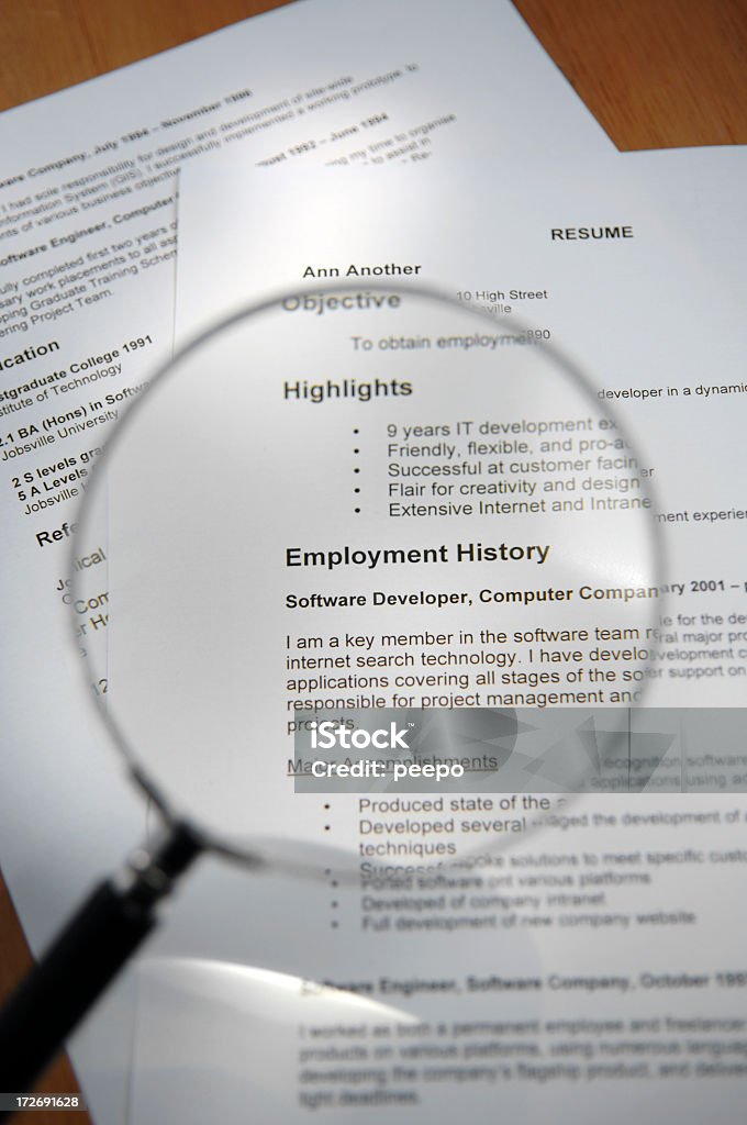 Magnifying Glass Over Resume A close up image of a magnifying glass placed over a two sheets of a generic resume loosely arranged on a wooden desk. The magnifying glass is over the “Highlights” and “Employment History” sections of the resume. Selective focus with the text under the magnifying glass in focus. All details are ficticious Résumé Stock Photo